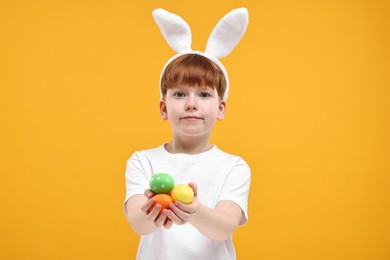 Photo of Easter celebration. Cute little boy with bunny ears and painted eggs on orange background