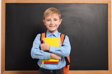Photo of Happy schoolboy with backpack and books near blackboard
