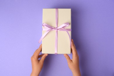 Photo of Child with gift box on light purple background, top view