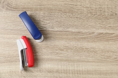 Photo of Color staplers on wooden table, flat lay. Space for text