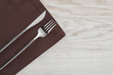 Photo of Fork, knife and napkin on white wooden table, top view with space for text. Stylish shiny cutlery set