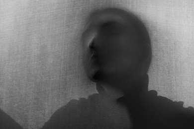 Photo of Silhouette of creepy ghost behind grey cloth. Black and white effect