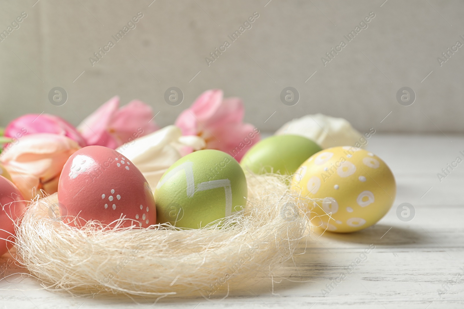 Photo of Sisal nest and painted Easter eggs on wooden table, space for text