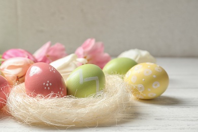 Photo of Sisal nest and painted Easter eggs on wooden table, space for text