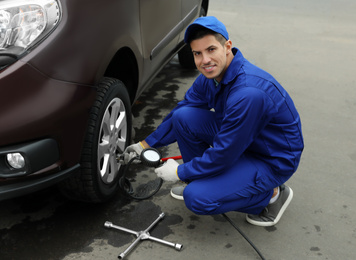 Photo of Worker checking tire pressure in car wheel at service station