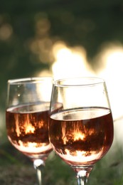 Photo of Glasses of tasty rose wine on blurred background, closeup. Picnic season