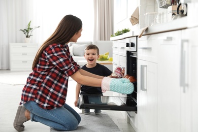 Son and mother taking out tray of baked buns from oven in kitchen