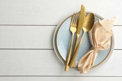 Photo of Stylish setting with cutlery, plates and napkin on white wooden table, top view. Space for text