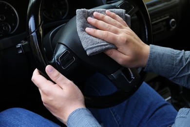 Photo of Man cleaning steering wheel with rag in car, closeup