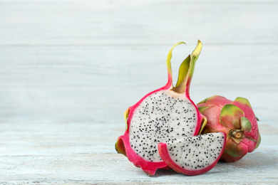 Photo of Delicious cut and whole dragon fruits (pitahaya) on light wooden table. Space for text