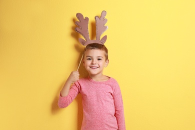 Image of Cute little boy with reindeer antlers prop on yellow background. Christmas celebration