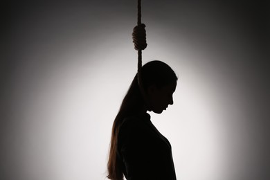 Photo of Silhouette of woman with rope noose on neck against light background