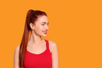 Photo of Happy woman with red dyed hair on orange background, space for text