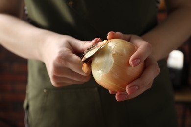 Photo of Woman peeling fresh onion with knife indoors, closeup
