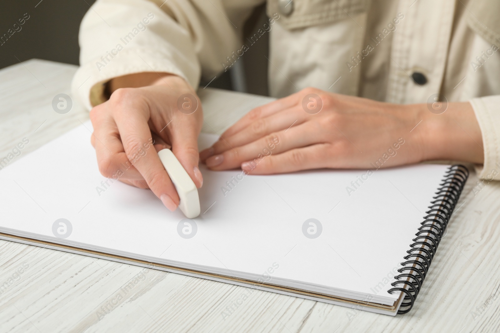 Photo of Woman erasing something in notebook at white wooden table, closeup