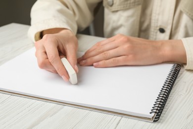 Photo of Woman erasing something in notebook at white wooden table, closeup