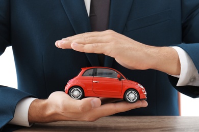Photo of Insurance agent holding toy car over table, focus on hands