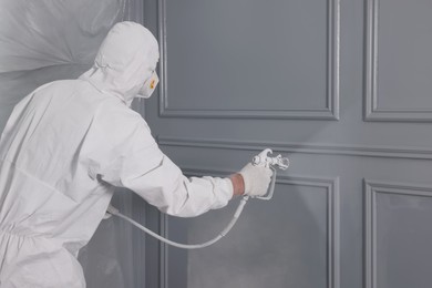 Photo of Decorator dyeing wall in grey color with spray paint, space for text