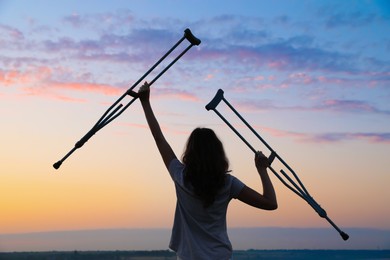 Photo of Woman holding axillary crutches outdoors at sunrise, back view. Healing miracle