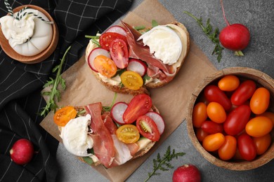 Photo of Delicious sandwiches with burrata cheese, ham, radish and tomatoes served on brown textured table, flat lay