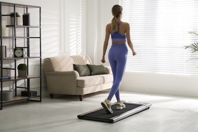 Photo of Sporty woman training on walking treadmill at home, back view