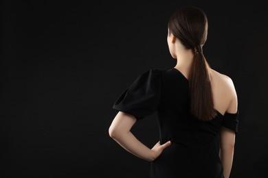Photo of Woman in elegant dress on black background, back view. Space for text