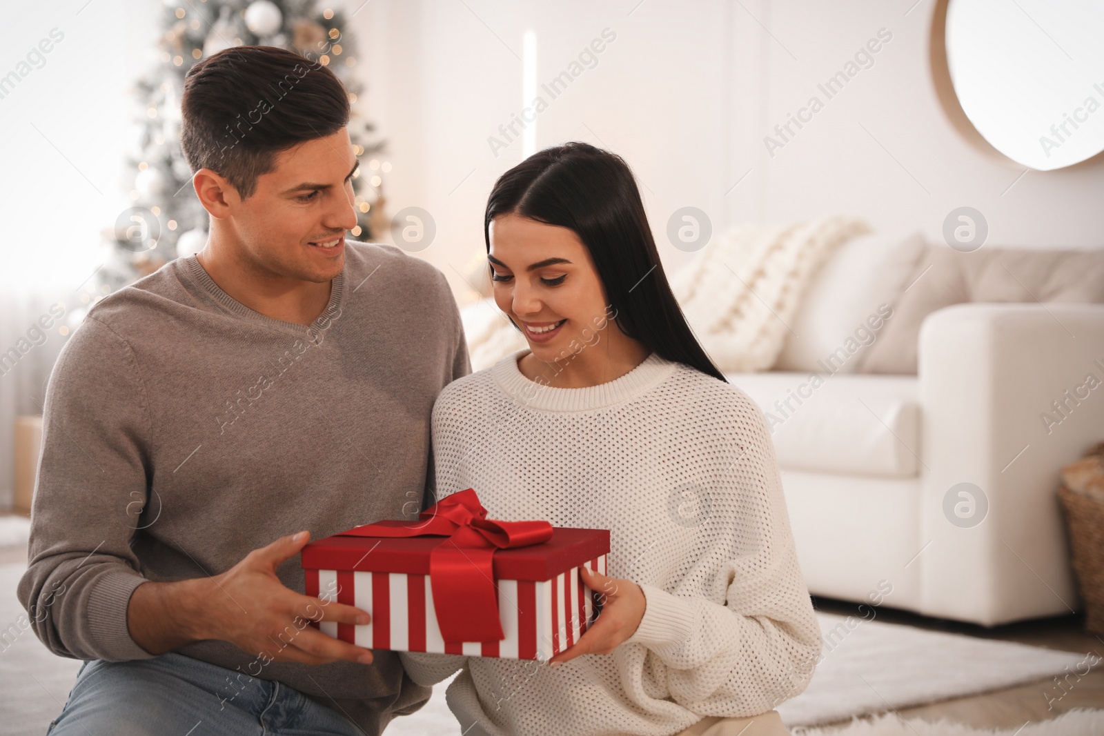 Photo of Couple holding gift box in room with Christmas tree