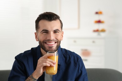 Photo of Handsome man with delicious smoothie at home. Space for text