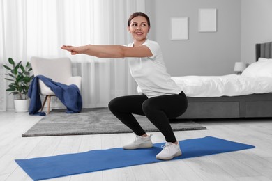 Photo of Morning exercise. Happy woman squatting at home