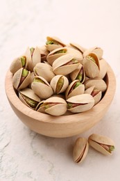 Photo of Delicious pistachios in bowl on white textured table