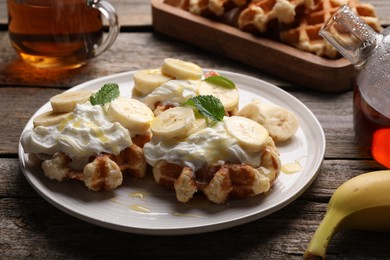 Photo of Delicious Belgian waffles with banana and whipped cream served on wooden table