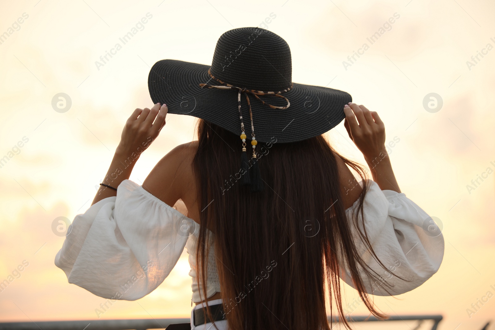 Photo of Young woman in hat at sunset, back view