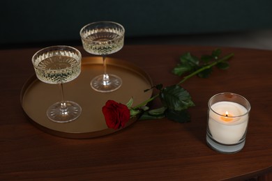 Photo of Burning candle, glasses of wine and beautiful red rose on wooden table indoors