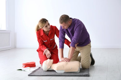 Photo of Instructor and man practicing first aid on mannequin indoors