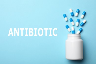 Image of Word Antibiotic and bottle with pills on light blue background, flat lay