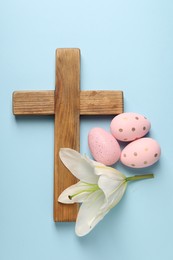 Photo of Wooden cross, painted Easter eggs and lily flower on light blue background, top view