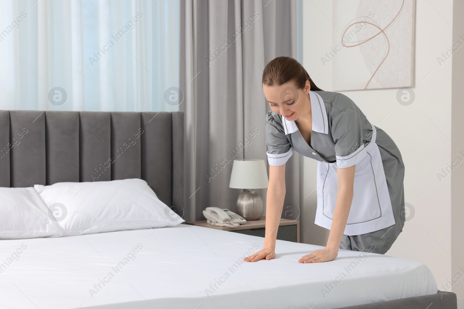 Photo of Young maid making bed in hotel room. Space for text