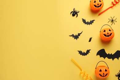 Photo of Flat lay composition with plastic pumpkin baskets, bats and straws on pale yellow background, space for text. Halloween celebration