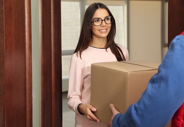 Photo of Woman receiving parcel from delivery service courier indoors