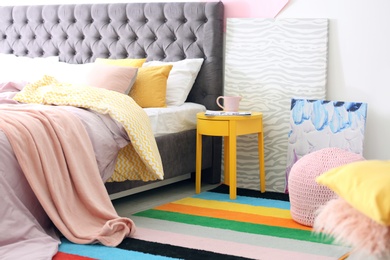 Photo of Stylish room interior with comfortable bed and rainbow carpet