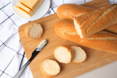 Photo of Tasty cut baguette with fresh butter on white table, flat lay