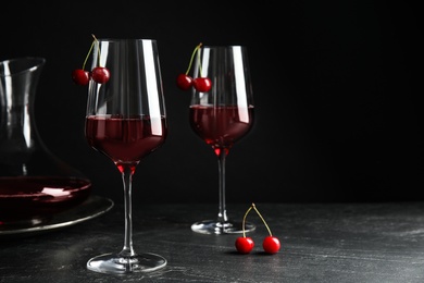Photo of Delicious cherry wine with ripe juicy berries on grey table against black background. Space for text