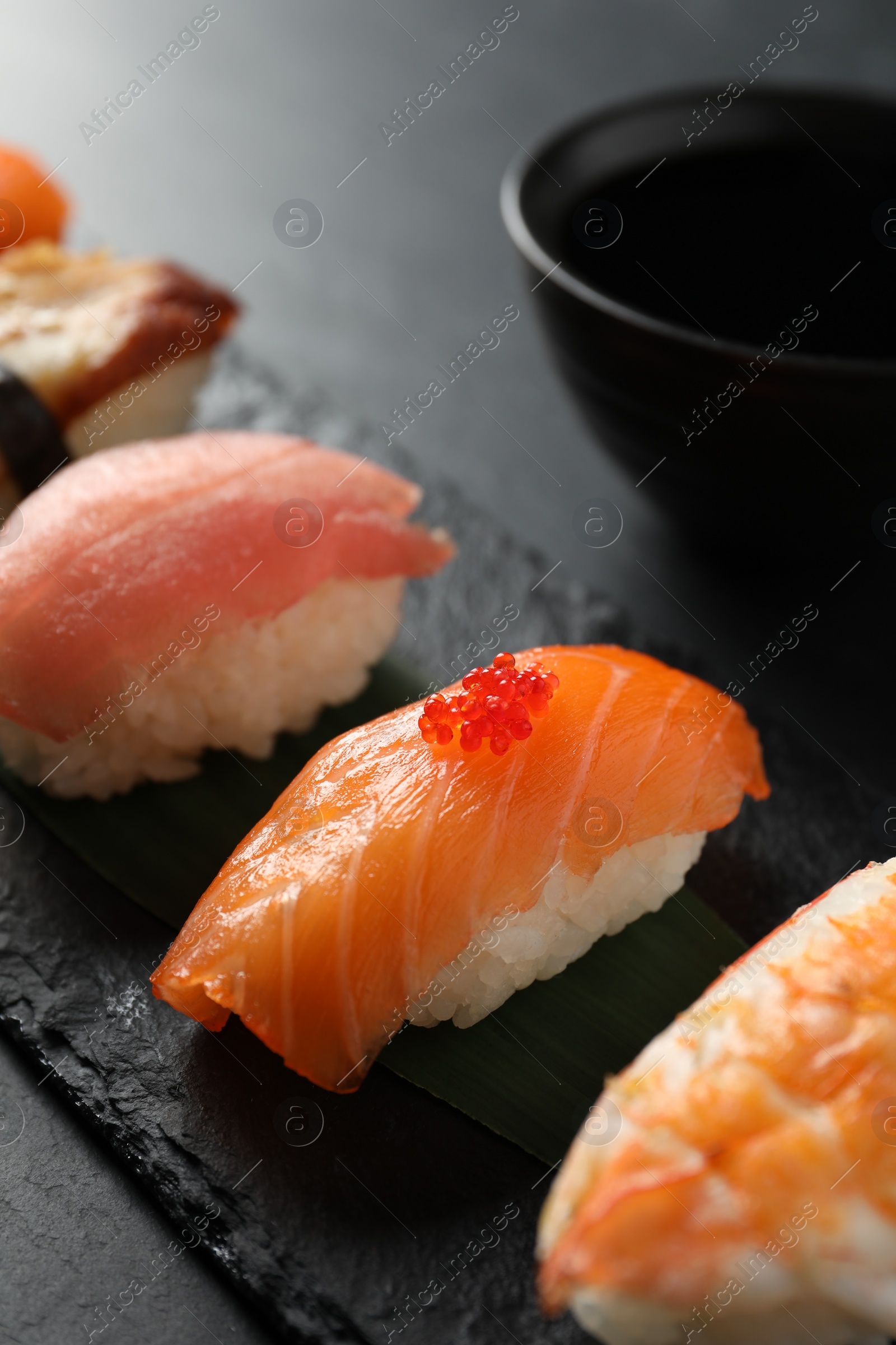 Photo of Serving board with delicious nigiri sushi and soy sauce on black table, closeup