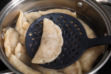 Photo of Boiling delicious dumplings (varenyky) on skimmer over pot, closeup