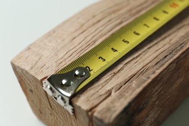 Photo of Tape measure on timber strip, closeup. Construction tool