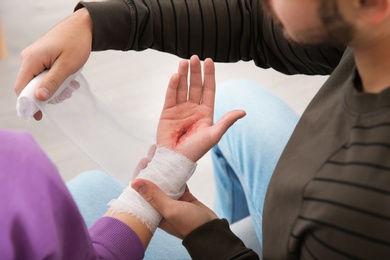 Photo of Young man applying bandage on woman's injured hand at home, closeup. First aid