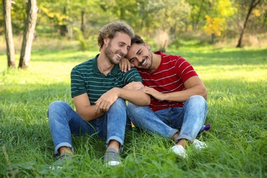 Photo of Portrait of happy gay couple sitting on grass in park