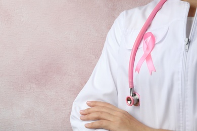 Photo of Doctor with pink ribbon and stethoscope on color background, space for text. Breast cancer awareness