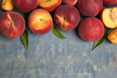 Photo of Fresh peaches and leaves on blue wooden table, top view with space for text