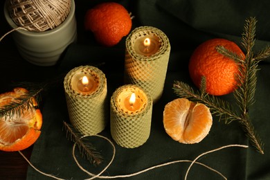 Beautiful burning beeswax candles, rope and tangerines on table, above view